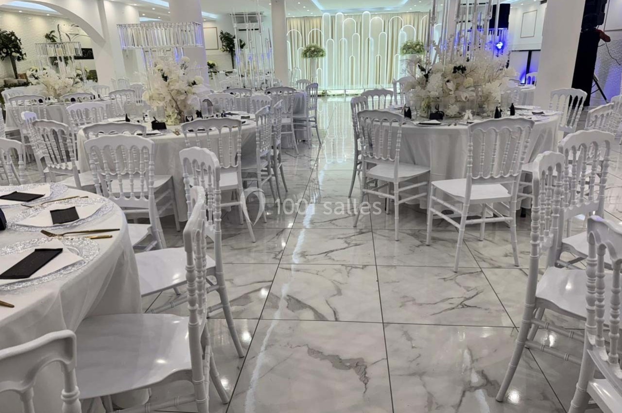 Salle de réception élégante avec tables rondes décorées de fleurs blanches et chaises blanches sur un sol en marbre.
