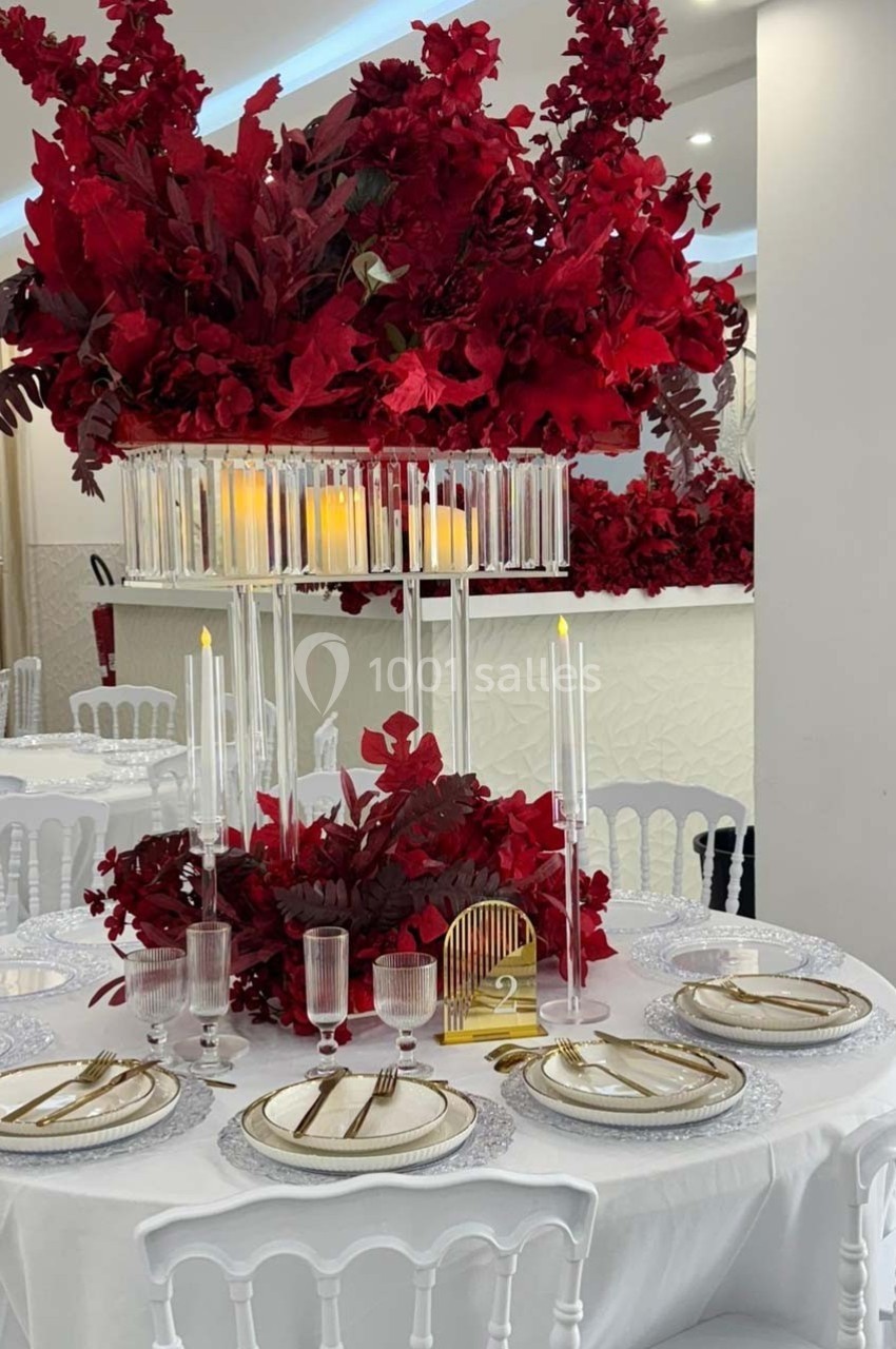 Table élégamment dressée avec vaisselle raffinée, bougies et centre de table composé de fleurs rouges abondantes.