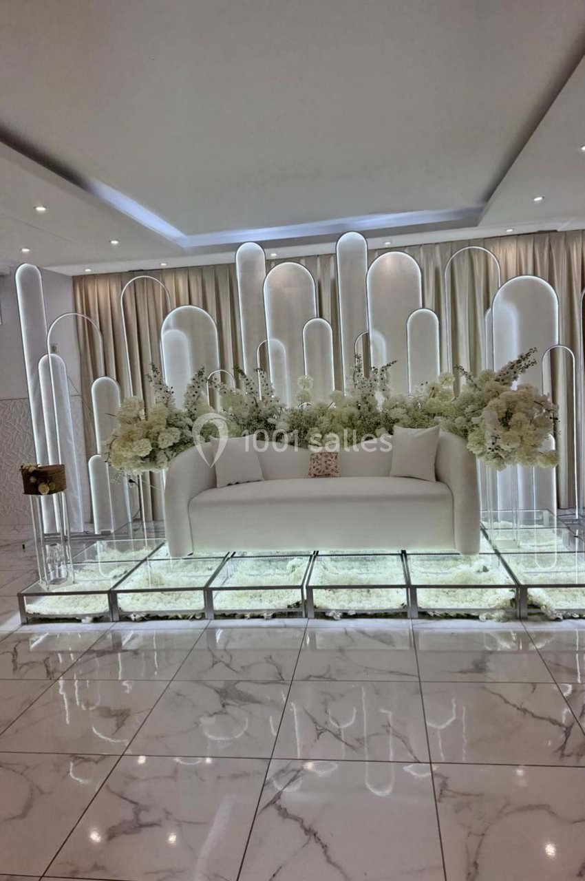 Canapé blanc entouré de colonnes lumineuses et de fleurs blanches, sur un sol en marbre brillant.