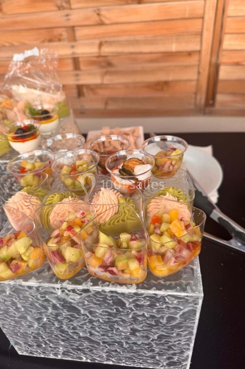 Verrines colorées de légumes et saumon disposées sur un présentoir en verre, avec d'autres amuse-bouches en arrière-plan.