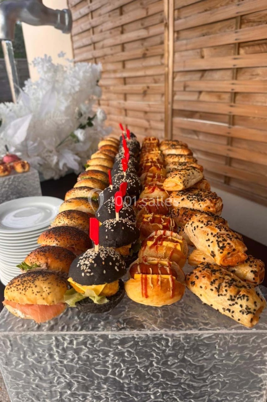 Plateau de mini-sandwichs variés et feuilletés garnis, disposés sur une table en extérieur avec une décoration blanche.