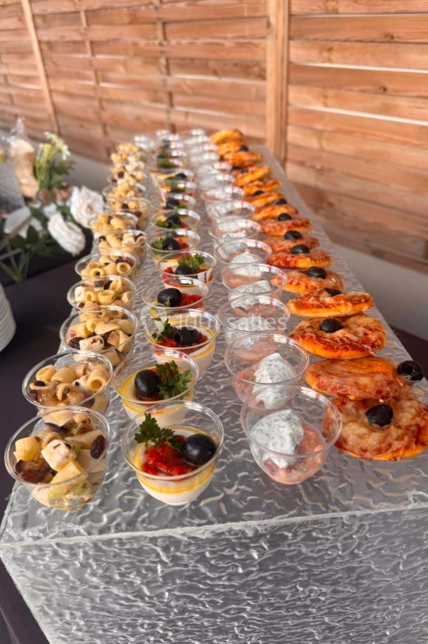 Buffet de verrines et amuse-bouches variés disposés en rangées sur une table avec fond en bois.