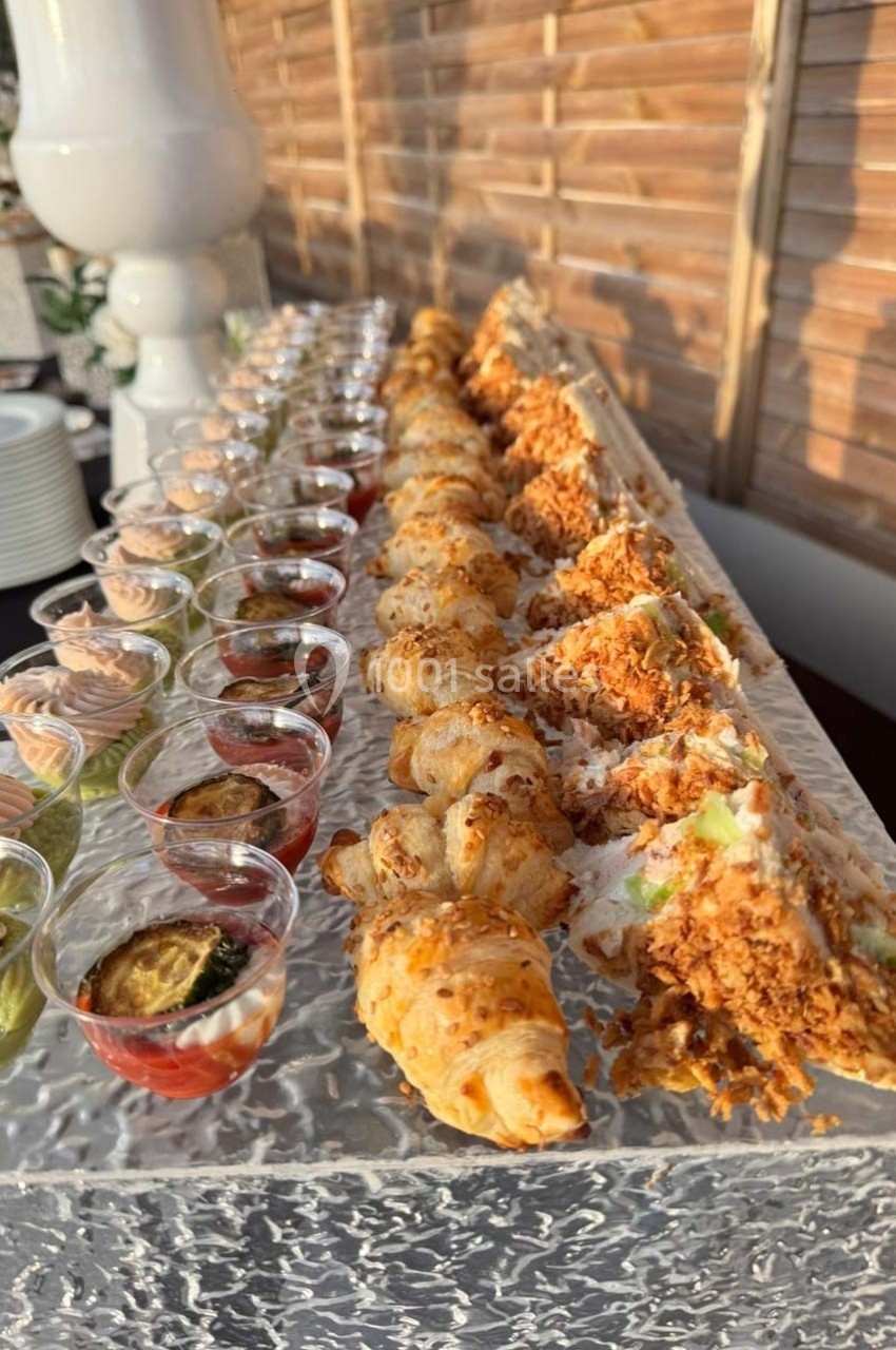 Plateau de bouchées apéritives comprenant mini-croissants, wraps garnis et verrines colorées sur une table.