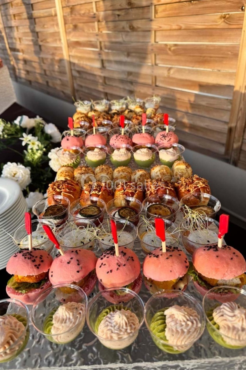 Plateau de bouchées apéritives variées, incluant mini-burgers et verrines, disposé sur une table en extérieur.