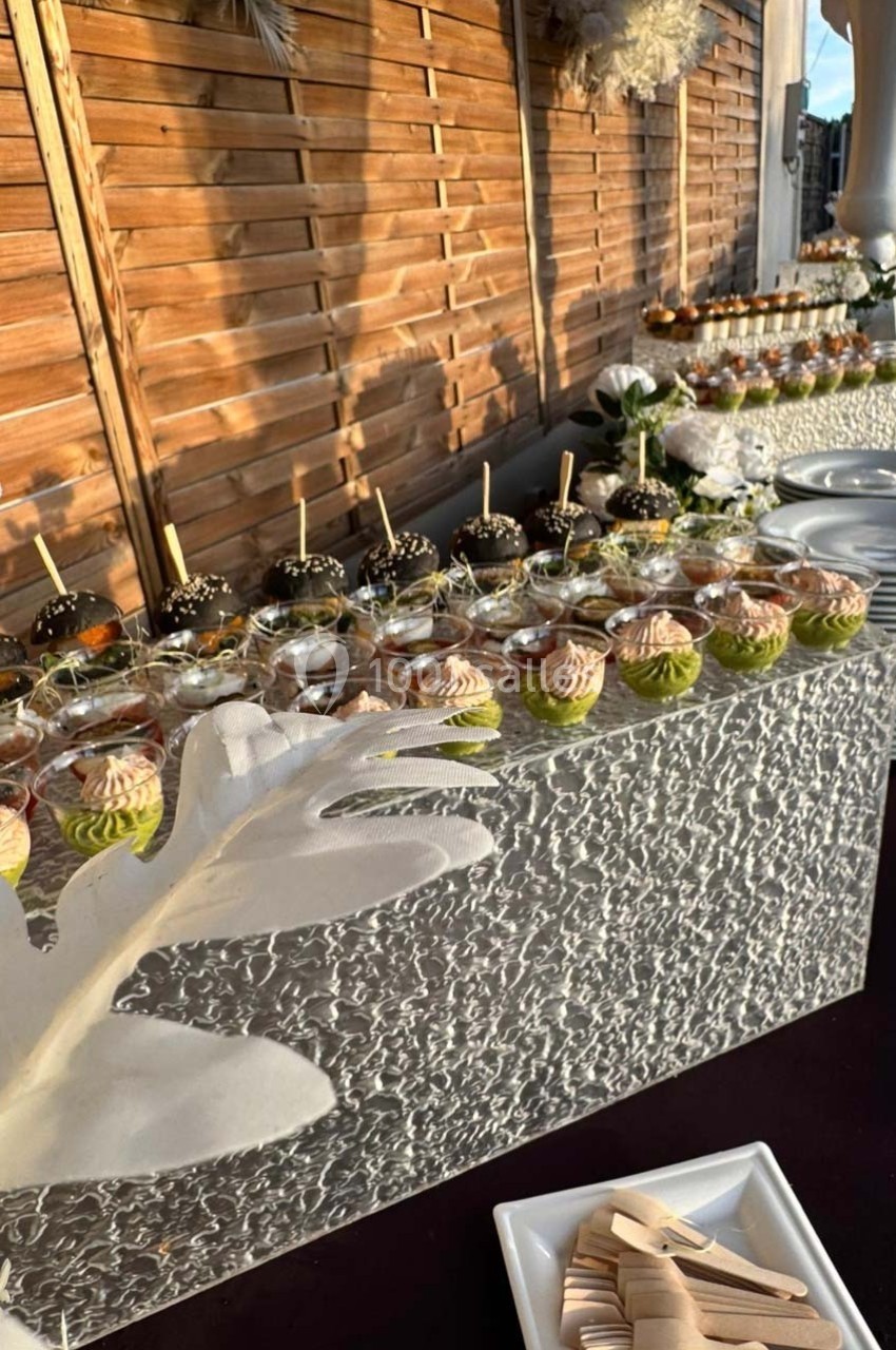 Buffet avec verrines colorées et desserts variés, disposés sur une table décorée, en extérieur près d'un mur en bois.