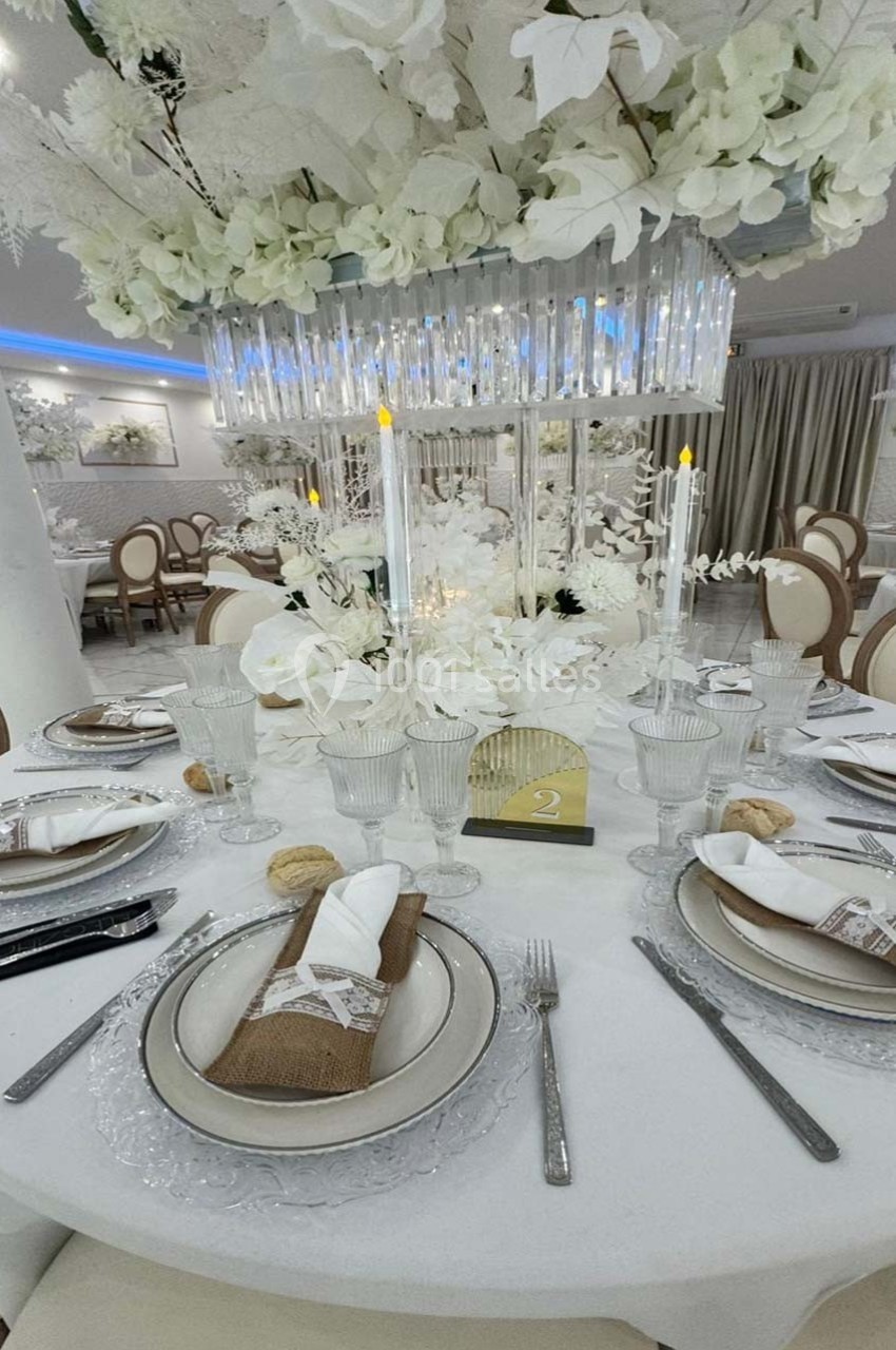 Table élégamment dressée avec vaisselle raffinée, décoration florale blanche et chandelier central lumineux.