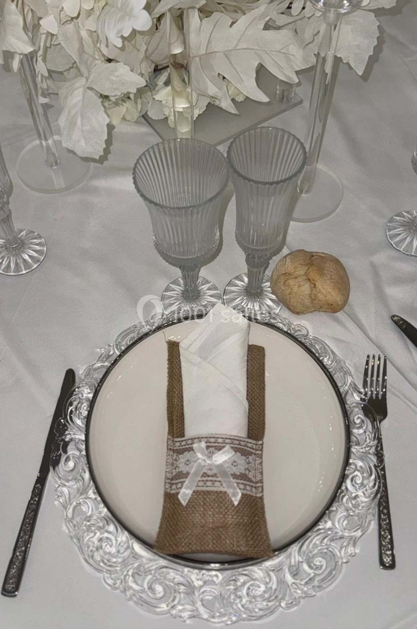 Table dressée avec assiette blanche sur un sous-plat décoré, serviette enroulée dans un étui en toile de jute, verres et…