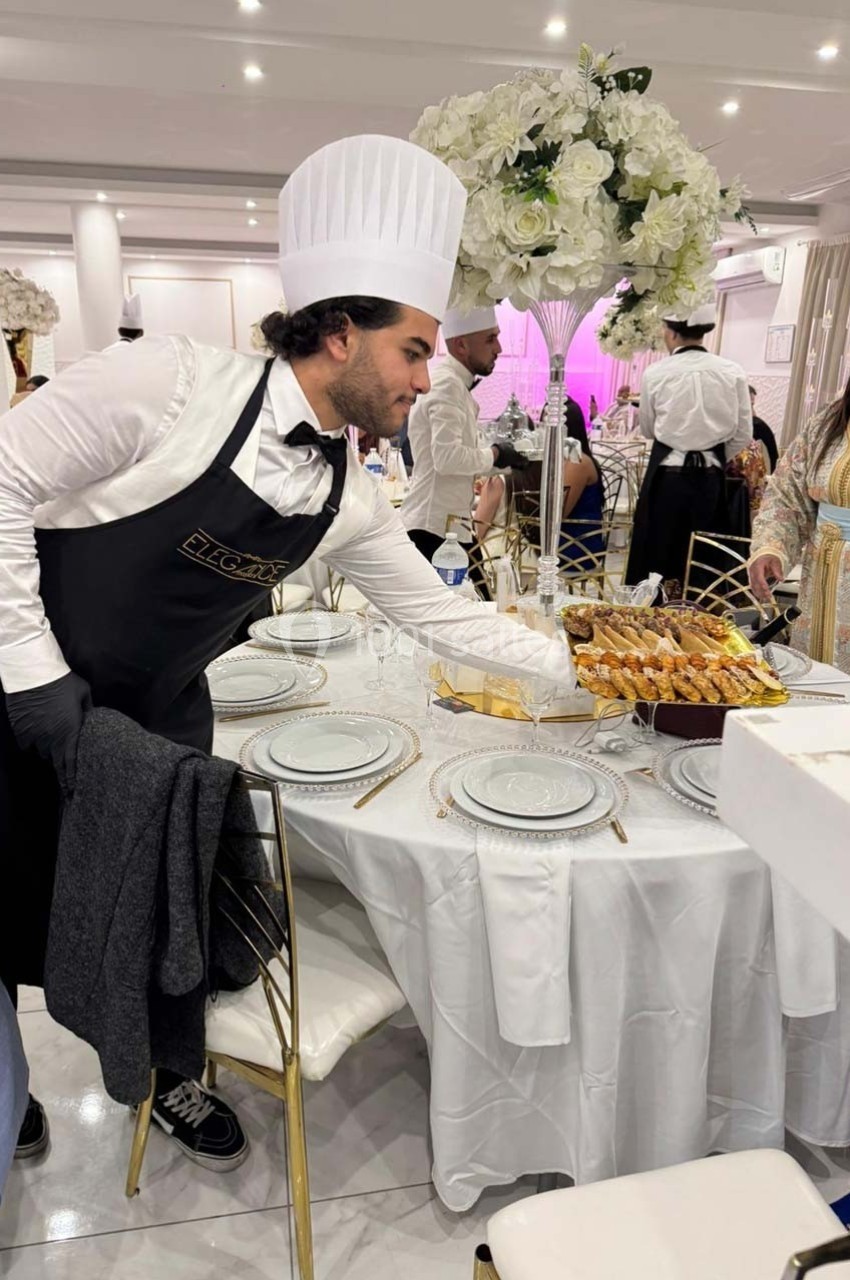 Un serveur en tenue de chef dispose des plats sur une table élégamment dressée pour un événement.