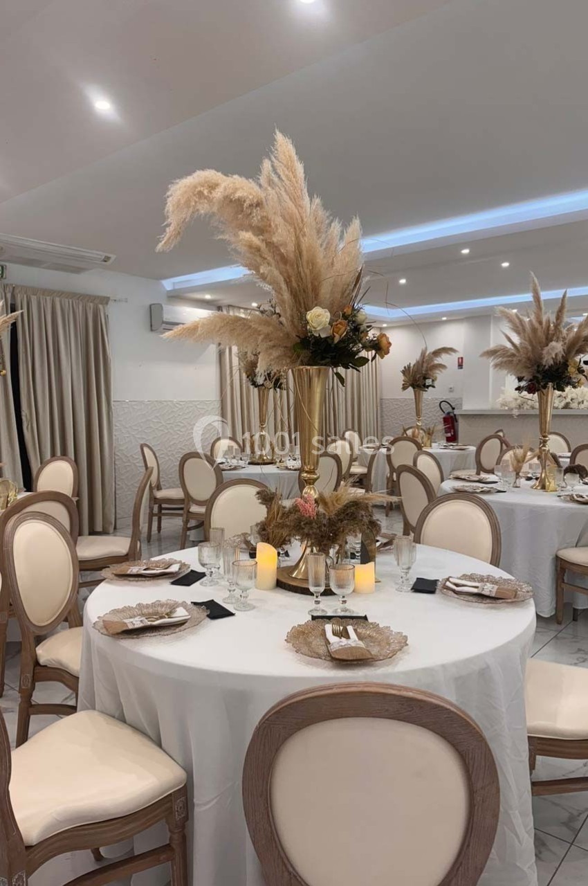 Salle de réception élégante avec tables rondes décorées de centres de table en pampas et bougies.