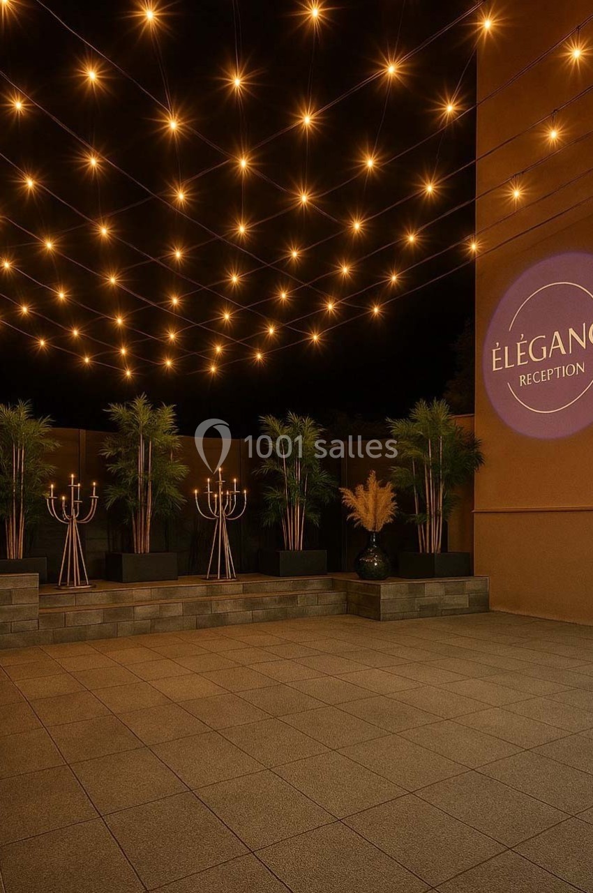 Guirlandes lumineuses suspendues au-dessus d'une terrasse avec plantes, chandeliers et un mur affichant ’Élégance Réception’.