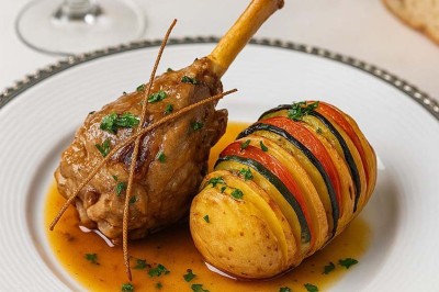 Assiette avec un jarret d'agneau en sauce et un millefeuille de légumes, servie sur une table dressée.