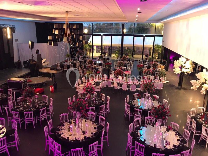 Salle de réception élégamment décorée avec des tables rondes, nappes noires, fleurs et éclairage tamisé.
