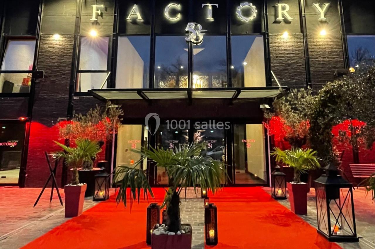 Entrée d'un bâtiment moderne avec façade noire, tapis rouge, plantes et éclairage nocturne.