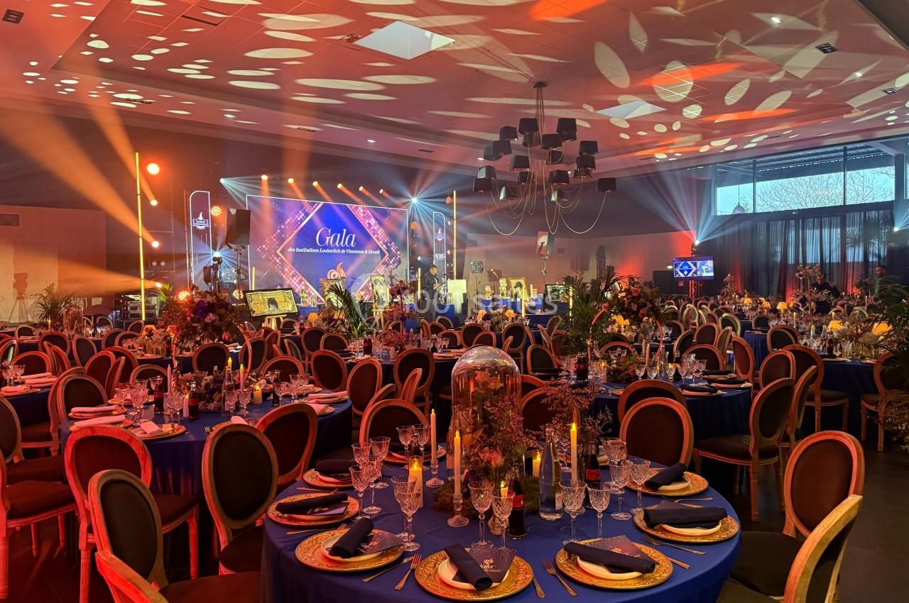 Salle de réception décorée pour un gala, avec tables dressées, éclairages colorés et ambiance festive.
