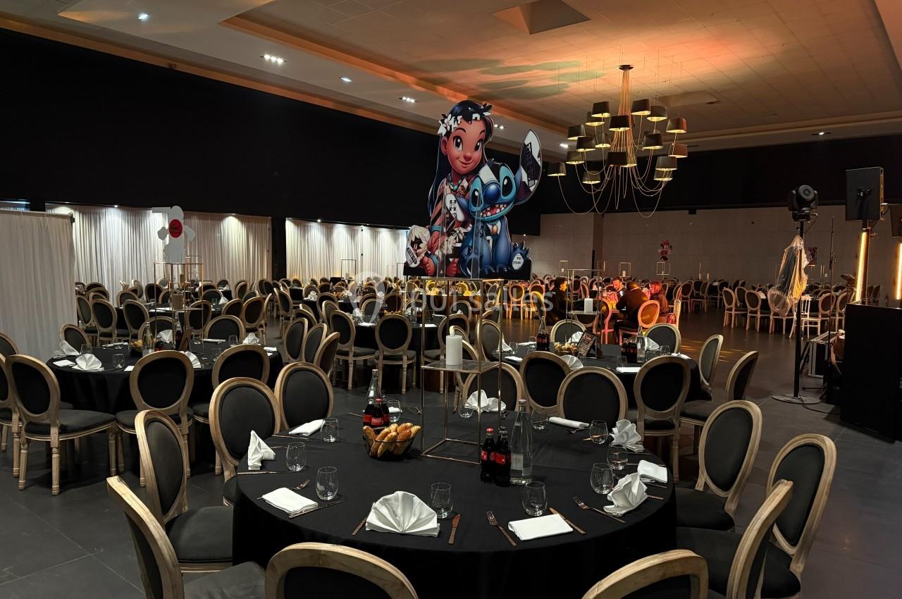 Salle de réception décorée avec des tables rondes dressées et une grande figurine colorée en arrière-plan.