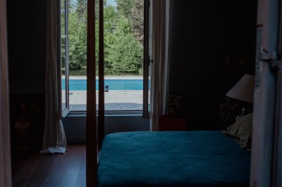 Miniature Chambre 1 Vue sur une piscine extérieure entourée de pelouse, avec un lac et des arbres en arrière-plan sous un ciel dégagé.