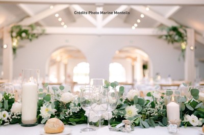 Table de réception élégamment dressée avec nappes blanches, verres, couverts, fleurs et bouteilles disposés harmonieusement.