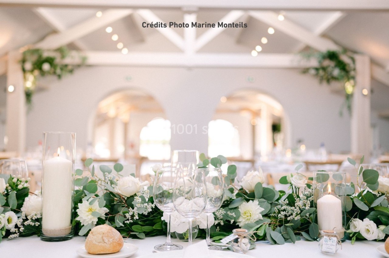 Table de réception élégamment décorée avec des fleurs blanches, des bougies et des éléments de vaisselle raffinée.