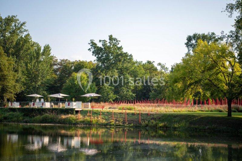 Terrasse avec parasols près d'un étang, entourée de végétation et de hautes herbes avec des tiges rouges décoratives.