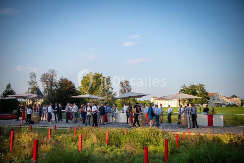 Groupe de personnes rassemblées en extérieur sur une terrasse avec parasols, entourée de végétation et bâtiments en arrière…