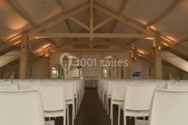 Salle de conférence lumineuse avec des rangées de chaises blanches et un écran de projection au fond.