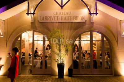 Façade éclairée du Château Larrivet Haut-Brion avec des invités visibles à travers les grandes fenêtres.