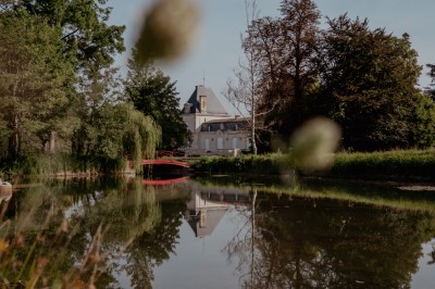 Bouteilles de vin rouge sur une table dressée avec des verres, des fleurs et une personne ajustant un couvert.