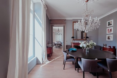 Bouteilles de vin rouge sur une table dressée avec des verres, des fleurs et une personne ajustant un couvert.