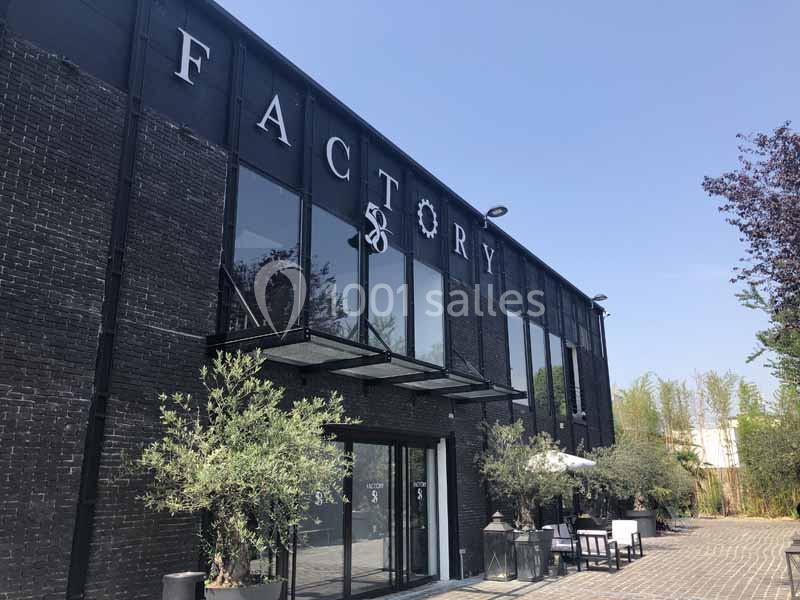 Façade d’un bâtiment industriel noir avec de grandes baies vitrées, marqué ’Factory 58’, entouré de végétation.