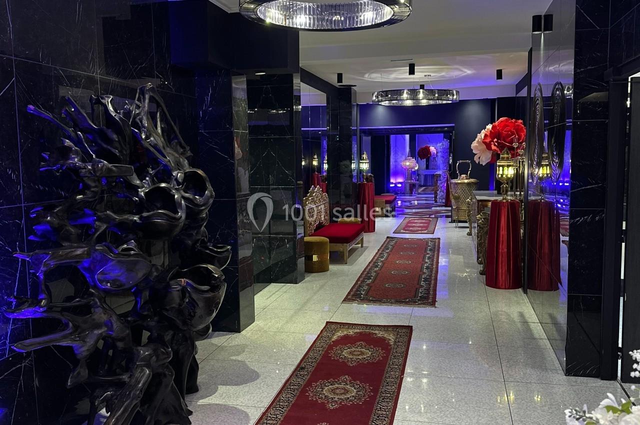 Couloir élégant avec tapis rouges, murs noirs brillants, éclairage bleu et lustre central en cristal.