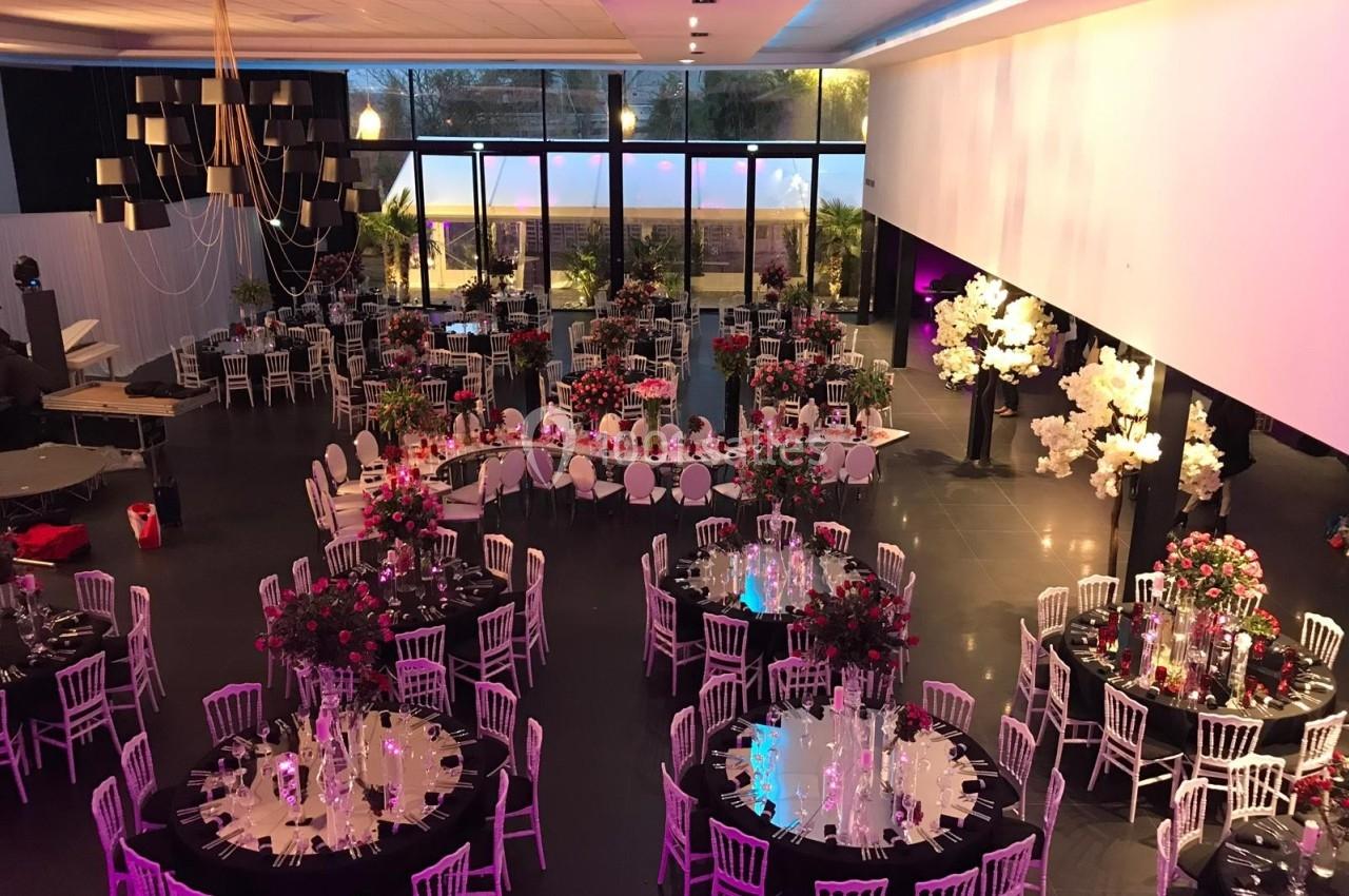 Salle de réception décorée avec des tables rondes, nappes noires, chaises blanches et arrangements floraux colorés.