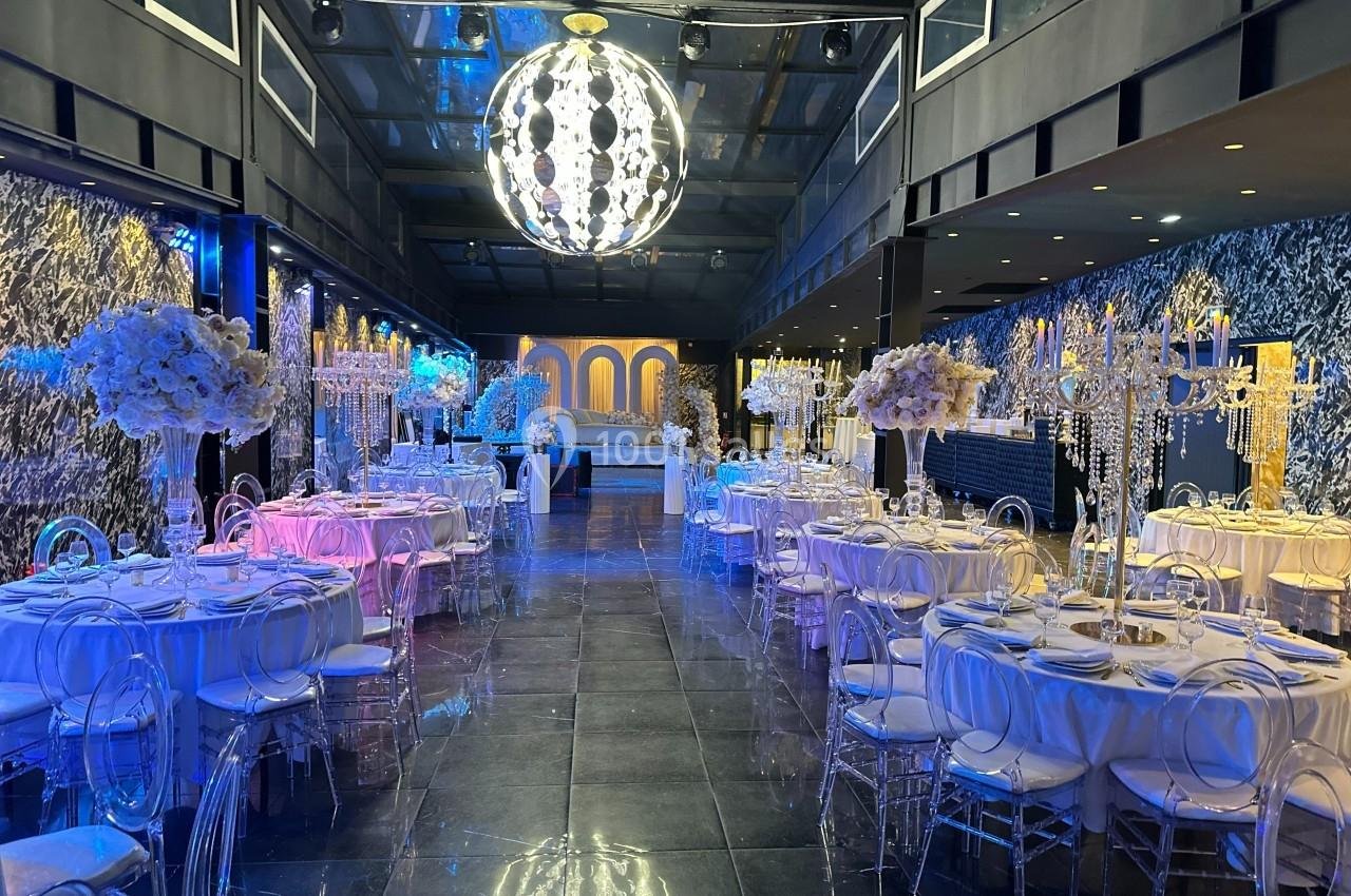 Salle de réception élégante avec tables décorées, chandeliers et éclairage coloré sous un grand lustre central.
