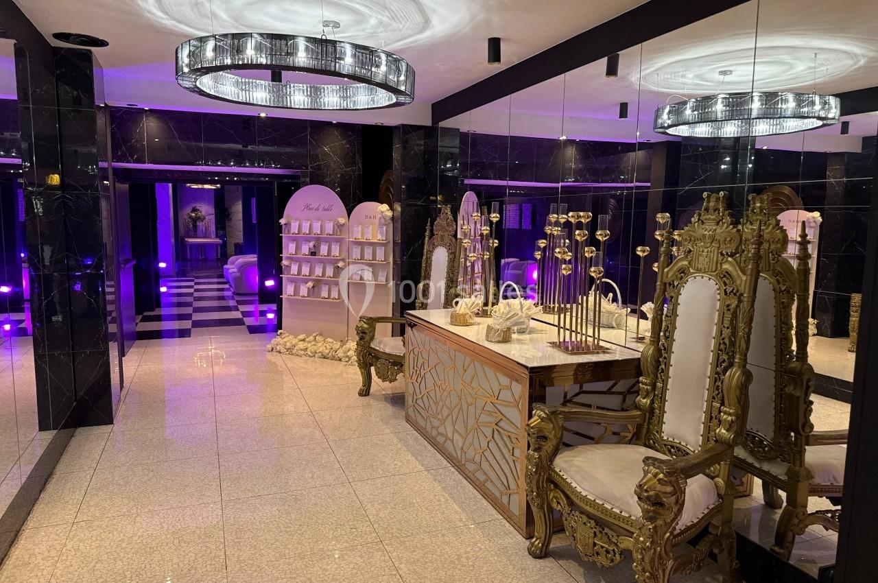 Salle luxueuse avec mobilier doré, lustres modernes, murs en miroir et éclairage violet tamisé.