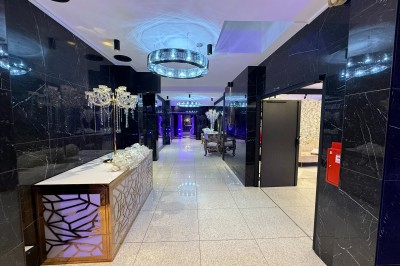 Miniature Location salle Bobigny (Seine-Saint-Denis) - Factory 58 #4 Salle de conférence moderne avec des rangées de chaises noires, sol en marbre et toit vitré laissant entrer la lumière…