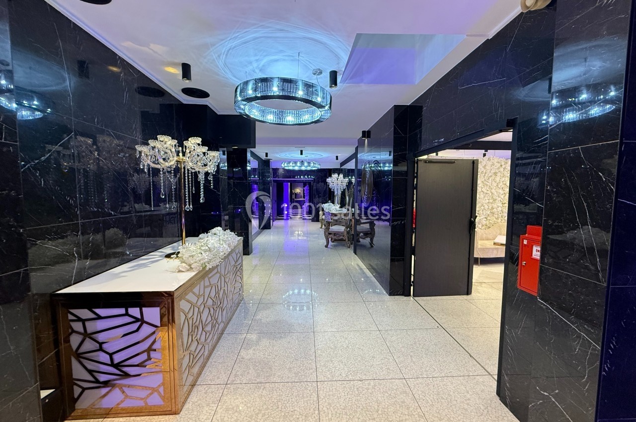 Location salle Bobigny (Seine-Saint-Denis) - Factory 58 #4 Hall moderne avec murs noirs brillants, sol en carrelage clair, lustre lumineux et mobilier élégant.