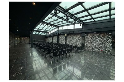 Miniature Location salle Bobigny (Seine-Saint-Denis) - Factory 58 #5 Salle de conférence moderne avec des rangées de chaises noires, sol en marbre et toit vitré laissant entrer la lumière…