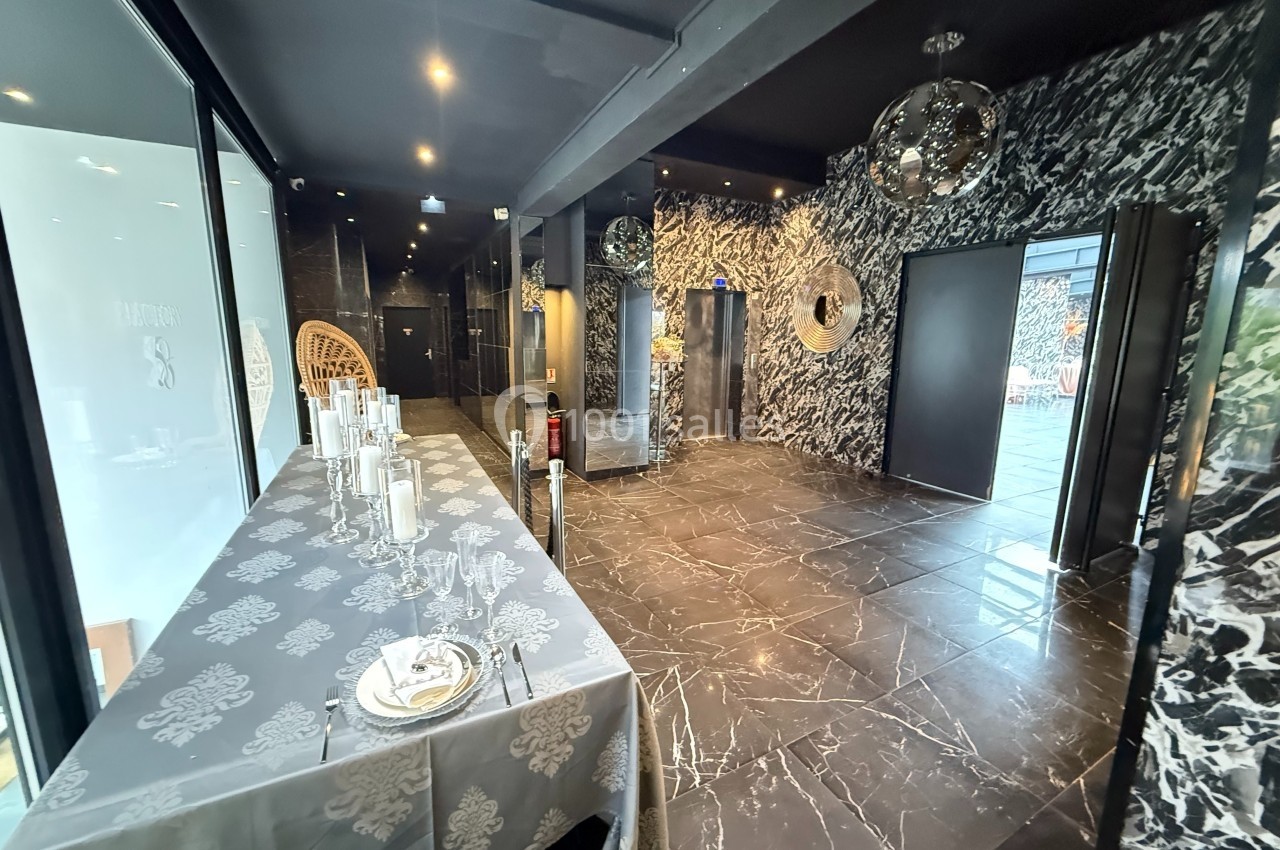 Lobby open sky Salle moderne avec sol en marbre noir, table dressée à gauche et décorations murales métalliques réfléchissantes.