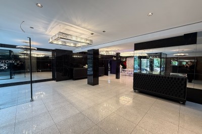 Miniature Loft villa Salle de conférence moderne avec des rangées de chaises noires, sol en marbre et toit vitré laissant entrer la lumière…