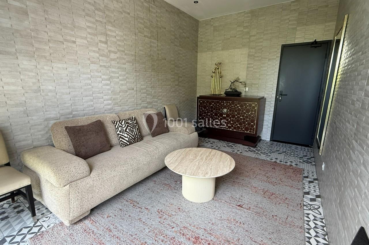 Loge villa Salon avec canapé beige, coussins décoratifs, table basse ronde, meuble en bois sculpté et sol en carreaux.