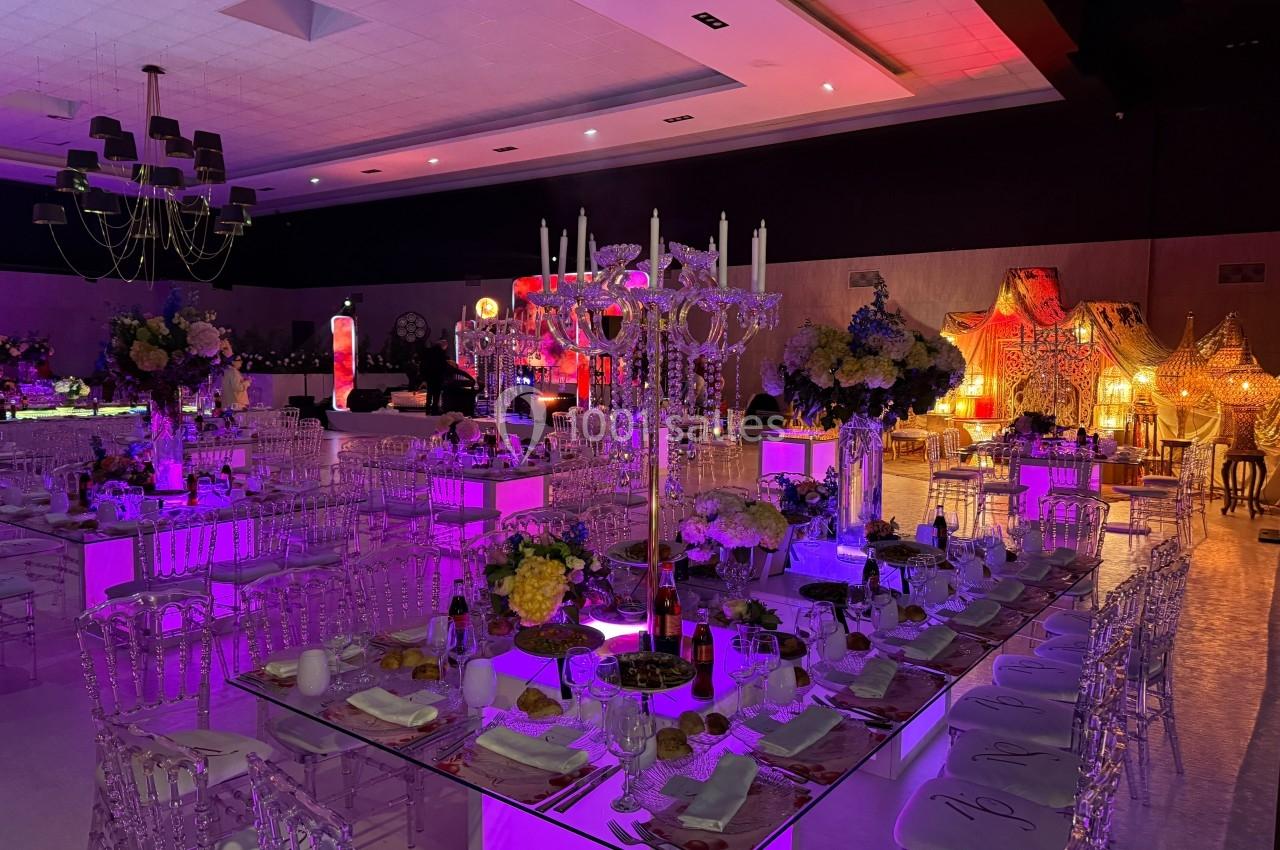 Soirée square Salle de réception décorée avec des tables illuminées, chaises transparentes et éclairage coloré.