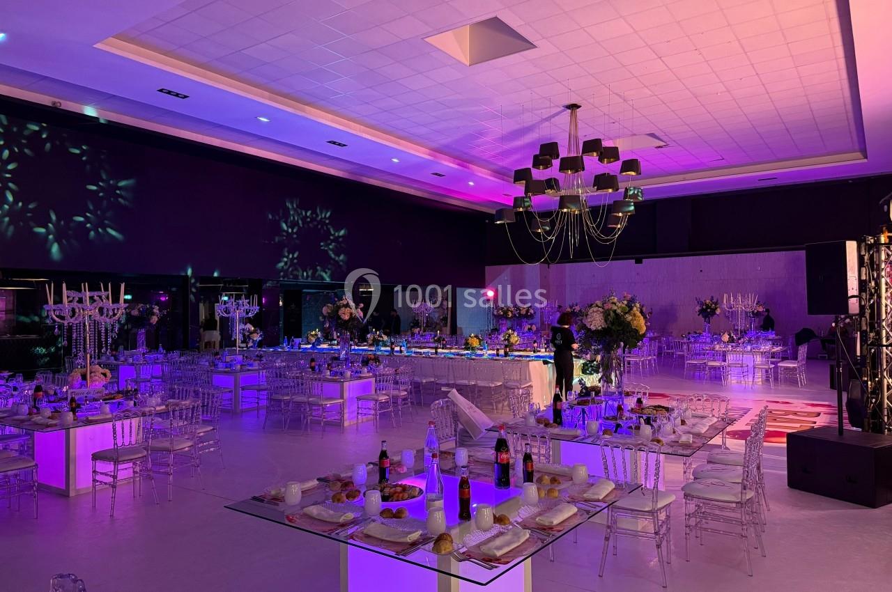 Soirée square Salle de réception décorée avec des tables dressées, éclairage coloré et ambiance festive.