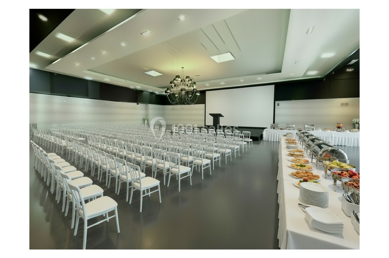 Square séminaire Salle de conférence avec rangées de chaises blanches, un podium, un écran de projection et un buffet dressé sur le côté.