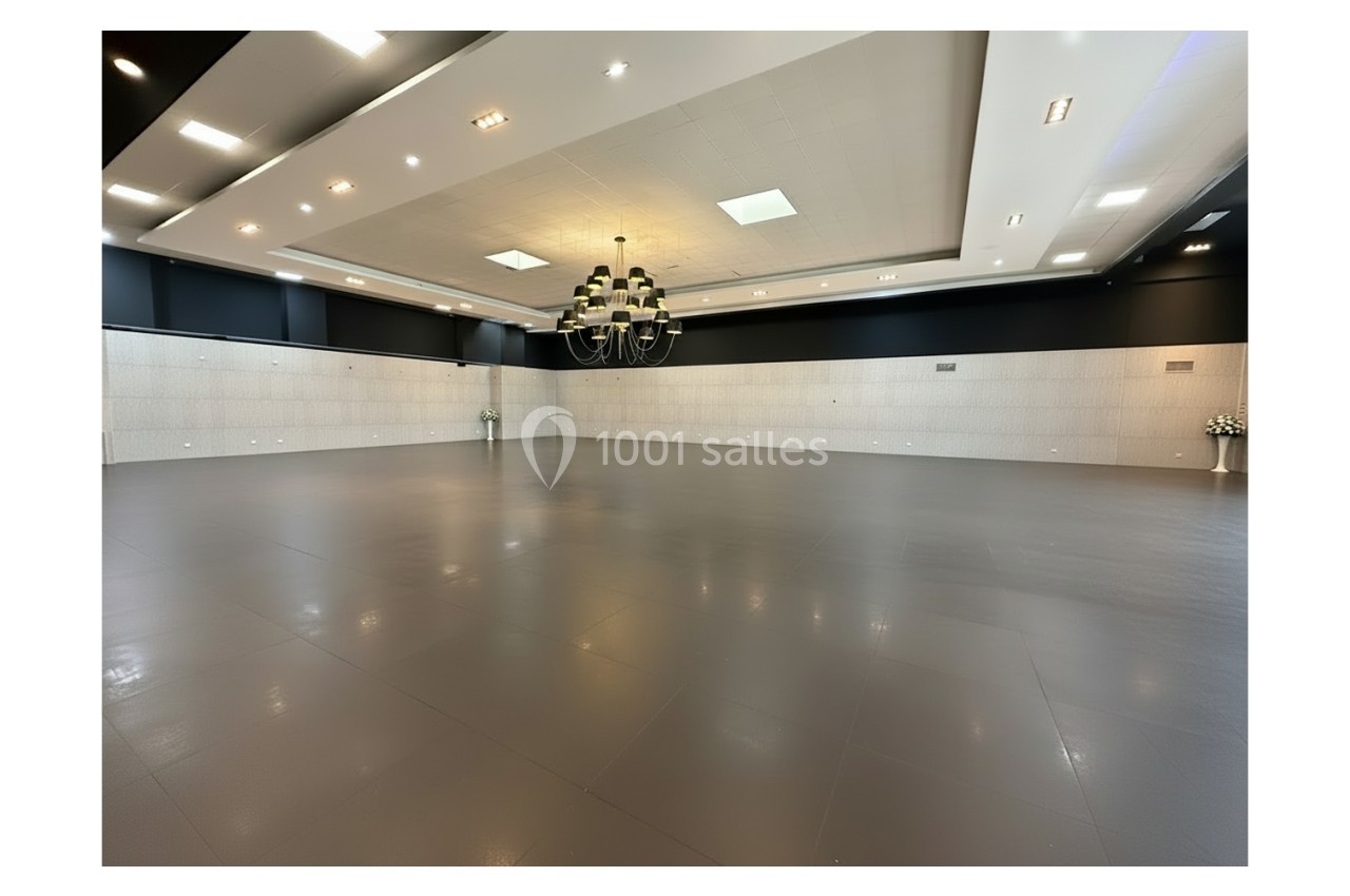 Square Salle spacieuse et vide avec un sol gris, un grand lustre central et des murs clairs ornés de panneaux.