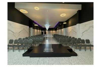 Miniature Villa format conférence Salle de conférence moderne avec des rangées de chaises noires, sol en marbre et toit vitré laissant entrer la lumière…