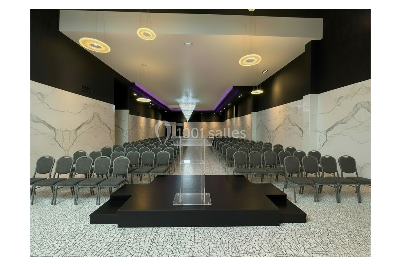 Villa format conférence Salle de conférence moderne avec rangées de chaises, estrade centrale et éclairage suspendu élégant.