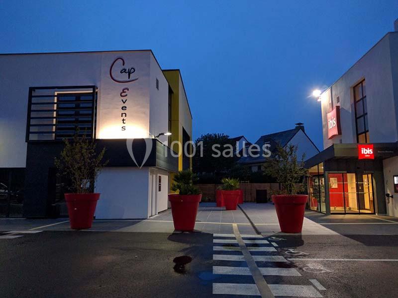 Façade d'un bâtiment Cap Events et entrée d'un hôtel Ibis éclairés à la tombée de la nuit.