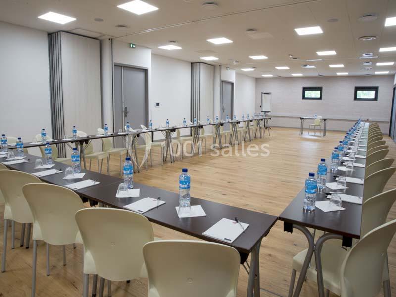 Salle de réunion lumineuse avec des tables disposées en U, équipées de bouteilles d'eau et de blocs-notes.