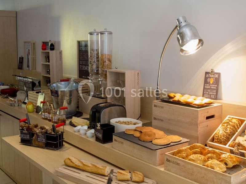 Buffet de petit-déjeuner avec viennoiseries, pain, céréales, fruits et boissons disposés sur un comptoir en bois.