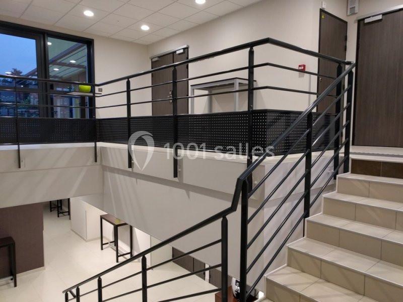 Escalier intérieur moderne avec rampe en métal noir, murs clairs et éclairage au plafond.