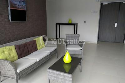 Salon moderne avec canapé, fauteuils en rotin, table basse en verre, décoration minimaliste et murs neutres.